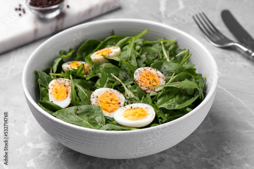 Delicious salad with boiled eggs and herbs in bowl on light grey marble table, closeup