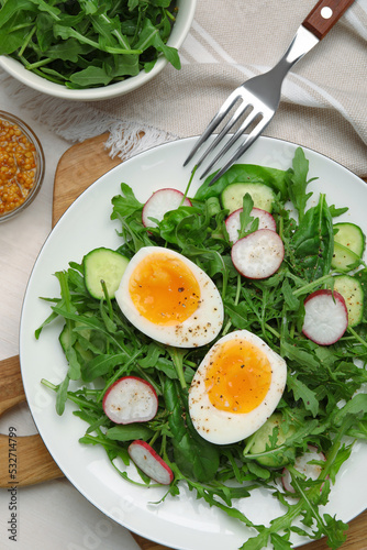 Delicious salad with boiled egg, vegetables and arugula served on white wooden table, flat lay