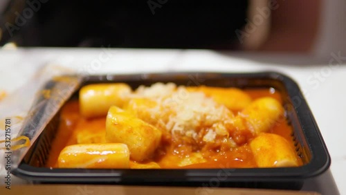 Woman's Hand Picks Korean Spicy Tteokbokki - Spicy Rice Cakes in Chili Sauce - close-up selective focus photo