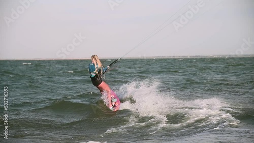 Slow motion on a telephoto lens. Young female athlete rides on a kiteboard in windy weather on big waves