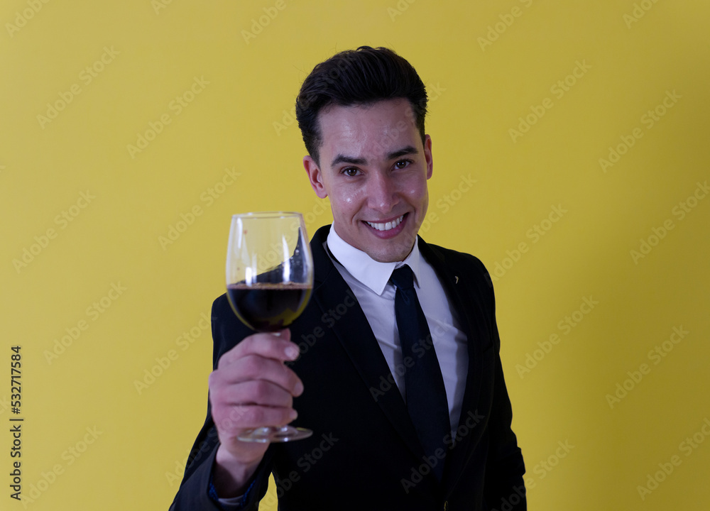Celebration, dinner, elegance, party! A smiling handsome guy dressed in formal suit holding a wine glass while looking at camera ahead a yellow background Celebration, dinner, elegance, party! A smiling handsome guy dressed in formal suit holding a wine glass while looking at camera ahead a yellow background