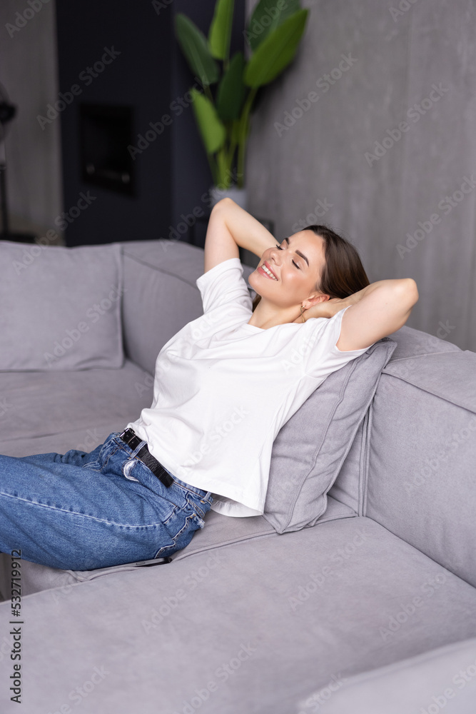 Relaxed peaceful woman relaxing on cozy couch in living room, satisfied young female with hands behind head leaning back on sofa Relaxed peaceful woman relaxing on cozy couch in living room, satisfied young female with hands behind head leaning back on sofa