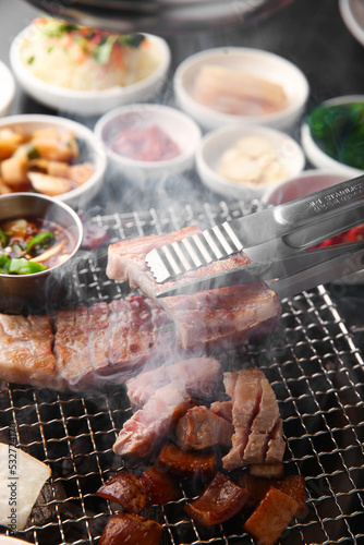 Grilled pork belly on a grill and set up a table with side dishes 그릴 위 노릇노릇하게 삼겹살을 굽고 있고 반찬이 세팅되어 있는 한상차림