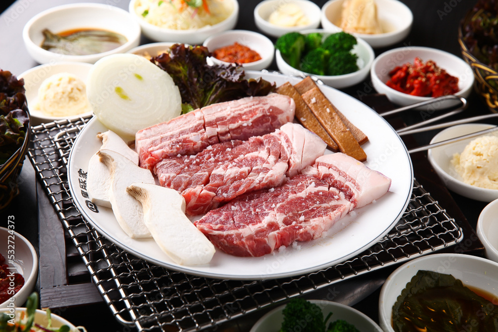 Korean table setting with grilled pork golden brown on the grill and side dishes set 그릴 위 노릇노릇하게 돼지고기를 굽고 있고 반찬이 세팅되어 있는 한상차림