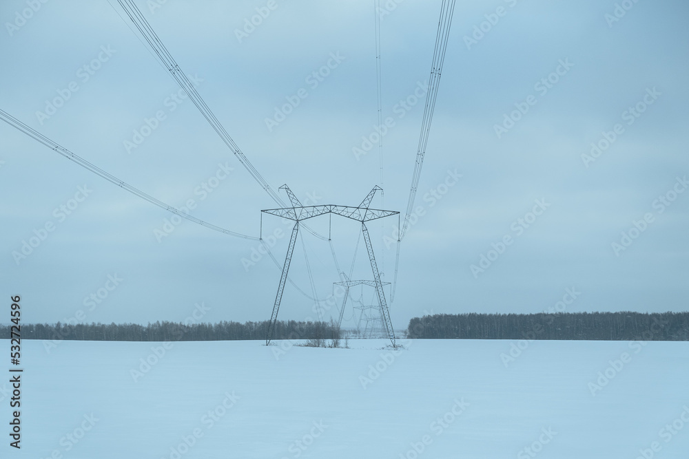 High-voltage poles winter. Electricity for cities. Electric pylons stand in the middle of a snow-covered field. The concept of heating, heating and alternative energy. Winter industrial landscape