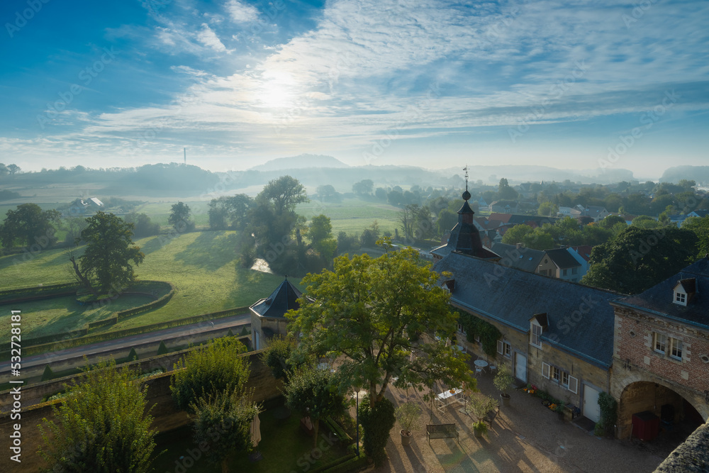 Overlooking the medieval chateau Neercanne, which serves as event venue outside Maastricht and a view over the Jeker valley which is covered in layers of mist during an autumn morning after sunrise