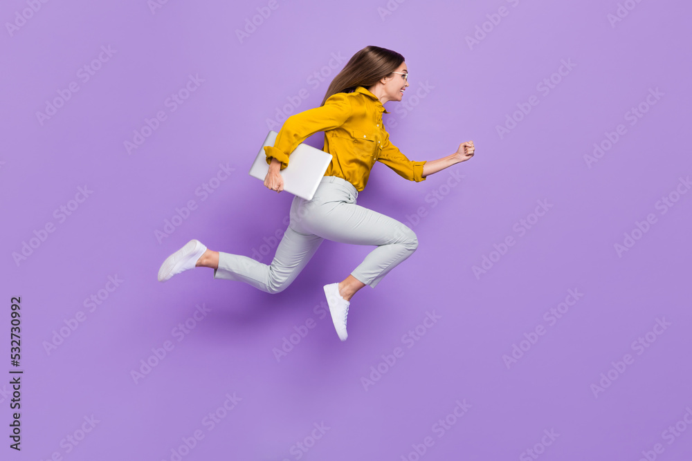 Full size profile portrait of crazy energetic girl hold netbook hurry rush jump empty space isolated on purple color background Full size profile portrait of crazy energetic girl hold netbook hurry rush jump empty space isolated on purple color background
