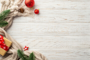 Winter holidays concept. Top view photo of red christmas decorations pine branches craft paper giftbox knitted scarf and anise on white wooden table background with copyspace