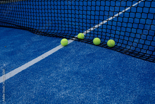 various balls by the net on a blue paddle tennis court © Vic