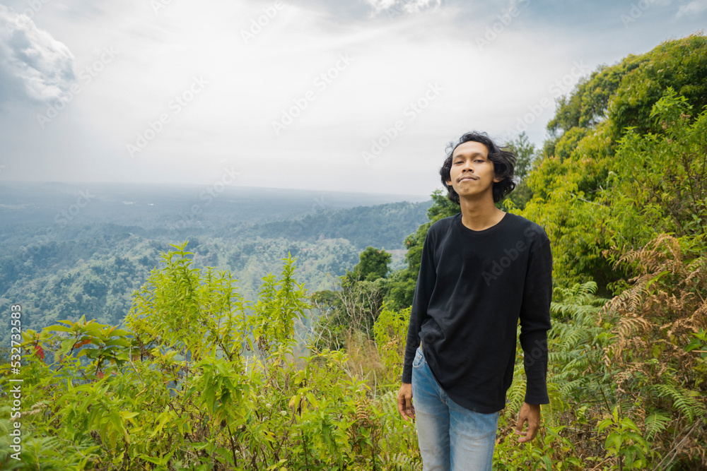 The young man smiling then stand and look on the peak of mountain. The photo is perfect for nature background, holiday poster and advertising.