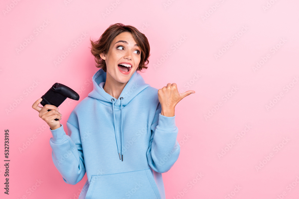 Photo of young adorable gorgeous cute woman wear blue hoodie hold joystick player online console finger pointing look empty space crazy isolated on pink color background Photo of young adorable gorgeous cute woman wear blue hoodie hold joystick player online console finger pointing look empty space crazy isolated on pink color background