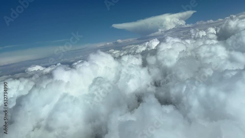 Impressive view from a jet cockpit during a right turn to avoid bad weather ahead, in a sky plenty of cumulus and a huge cumuloninbus anvil shape at the back. Pilot point of view. 4k photo