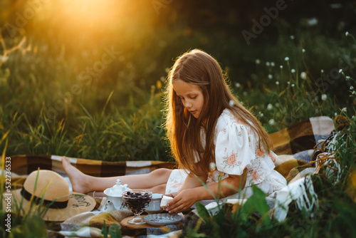 A girl is putting a piece of cake on herself during a picnic in the garden at sunset