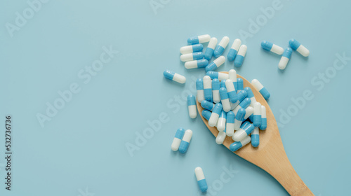 Blue-white antibiotic capsule pills on wooden spoon and blue background. Antibiotic drug resistance. Prescription drug. Medical care. Pharmaceutical care. Antimicrobial drug. World Pharmacist Day.