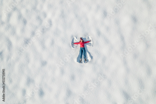 Woman lying on a snow and doing angel print on a snow covered land. Aerial, top view. Drone photo. Winter © flowertiare