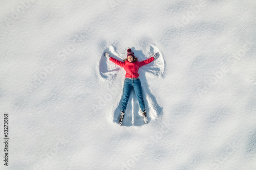 Woman lying on a snow and doing angel print on a snow covered land. Aerial, top view. Drone photo. Winter photo