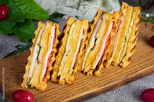Club sandwich with ham, cheese, tomato and salad. Grilled sandwich with dried tomatoes bread
