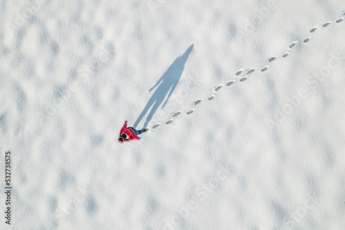 Woman in a red christmas jacket walking on the snow and doing footprints in a park. Winter. Drone, top, aerial view.
