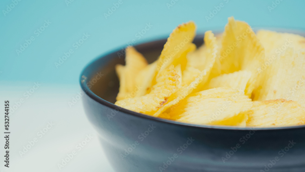 close up view of crunchy and ridged potato chips in bowl on blue with copy space. close up view of crunchy and ridged potato chips in bowl on blue with copy space.