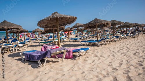 A Spanish beach in the summer, with rows of sun loungers and shades along the sand © parkerspics
