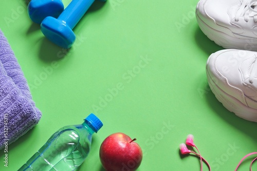 Fitness photography for banner design. Mockup, copy space. Towel, dumbbells, water bottle, apple, sneakers and pink headphones on a green background