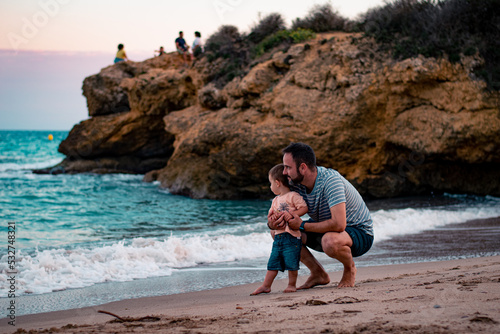 Papá e hijo bebé niño sonriente en la playa jugando y divirtiendose  photo