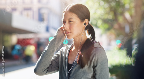 Asian woman, earphones and music streaming while in the city for travel, exercise or run on a sunny day. Calm female listening to podcast, radio or audio on an urban street or sidewalk in summer