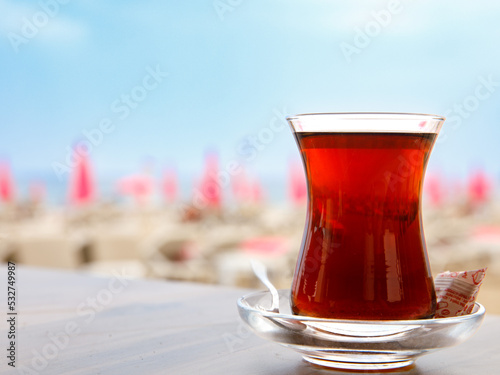Fototapeta Naklejka Na Ścianę i Meble -  Turkish tea in a traditional glass (tulip) Bardak against the background of beach. Holiday in Turkey, travel resort