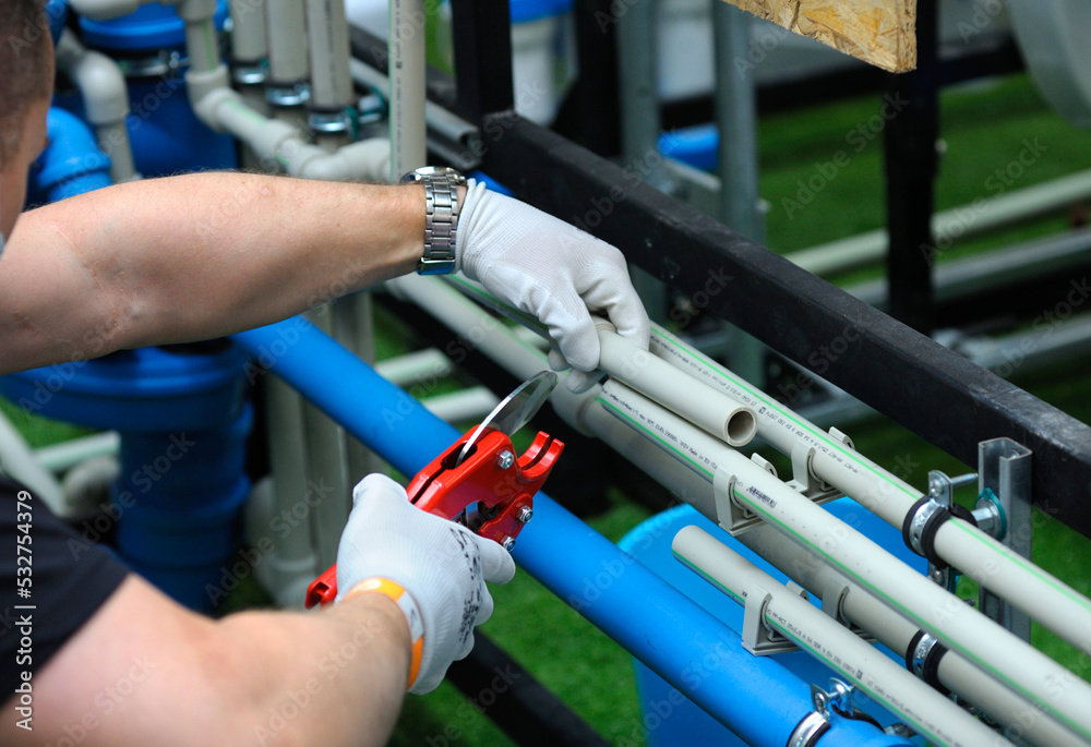 Plumber hands in gloves cut plastic pipe with the pipe cutter Plumber hands in gloves cut plastic pipe with the pipe cutter