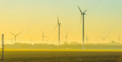 Wind turbines in a foggy agricultural field in sunlight at sunrise in autumn, Almere, Flevoland, Netherlands, September, 2022