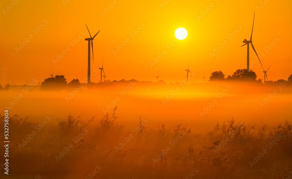 Obraz premium Wind turbines in a foggy agricultural field in sunlight at sunrise in autumn, Almere, Flevoland, Netherlands, September, 2022
