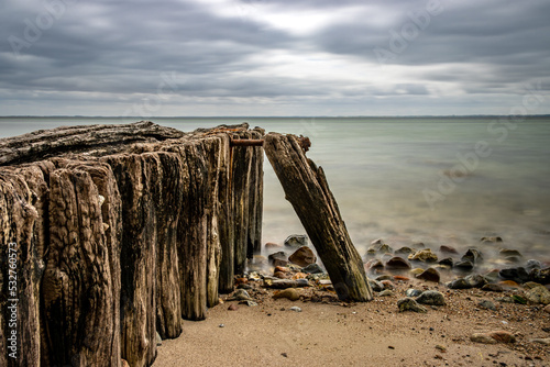 Beach on the Danish Baltic Sea near Sønderborg, Denmark. cloudy sky. In the foreground pier leads into the sea photo