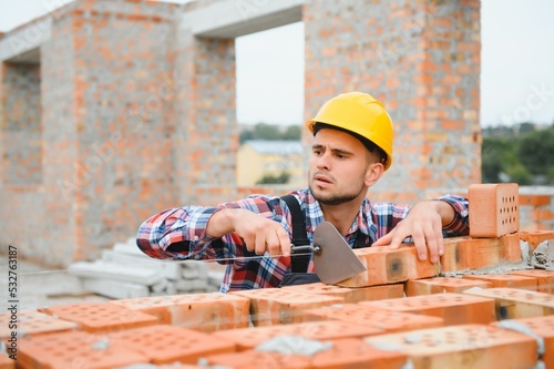 Yellow colored hard hat. Young man working in uniform at construction at daytime.