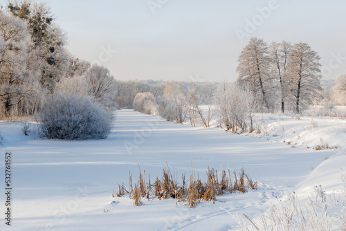 The frozen river is covered with ice and snow, the trees are covered with frost