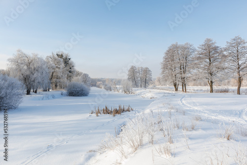 The frozen river is covered with ice and snow, the trees are covered with frost