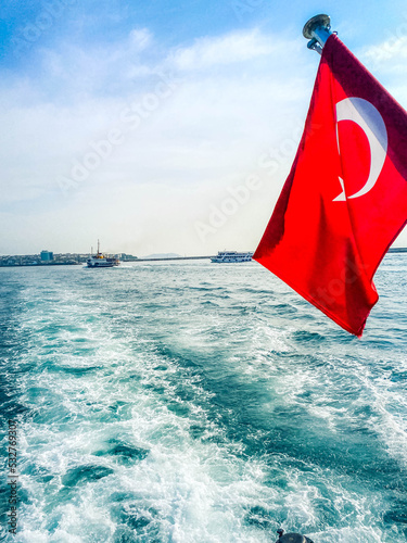 Istanbul, Turkey, OIctober 11, 2021. View of a ferry boat, historical mosques in Eminonu area and many people in Istanbul. It is a sunny summer day. Turkish flag waving on the ferry.