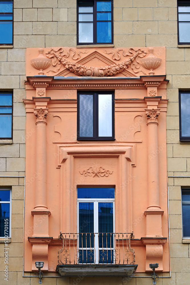 Balcony with columns on facade of old residential building decorated with bas-reliefs. Stalinist architecture, Stalin Empire style. Balcony and windows of soviet building.