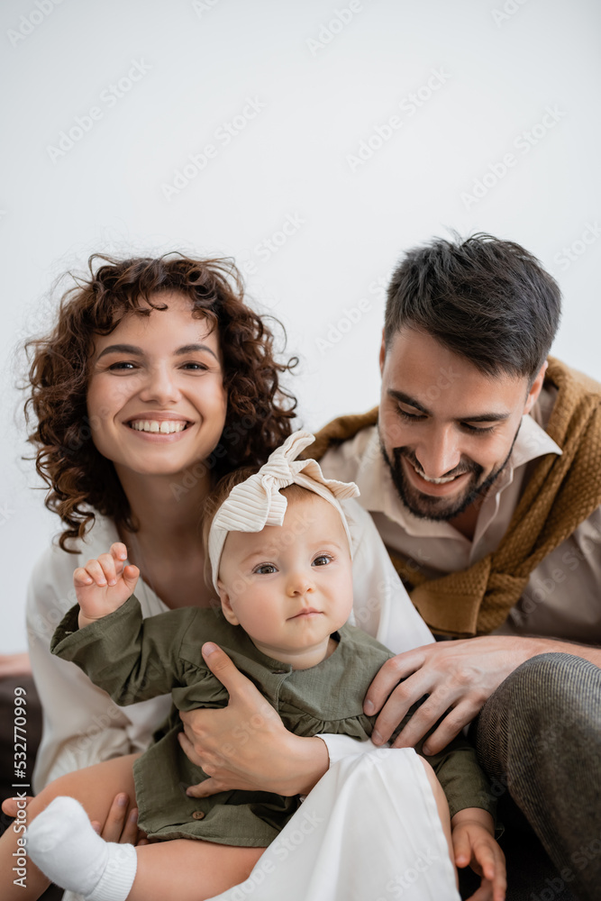 positive parents holding infant girl in headband and smiling in living room. positive parents holding infant girl in headband and smiling in living room.