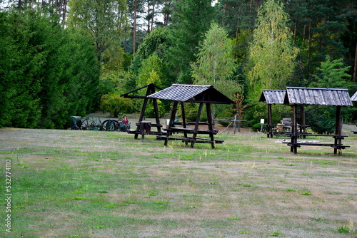 A close up on a camping spot with numerous shacks, shelters or huts made out of wooden logs and planks, with some firewood waiting for tourists and with sticks to be used for cooking sausages