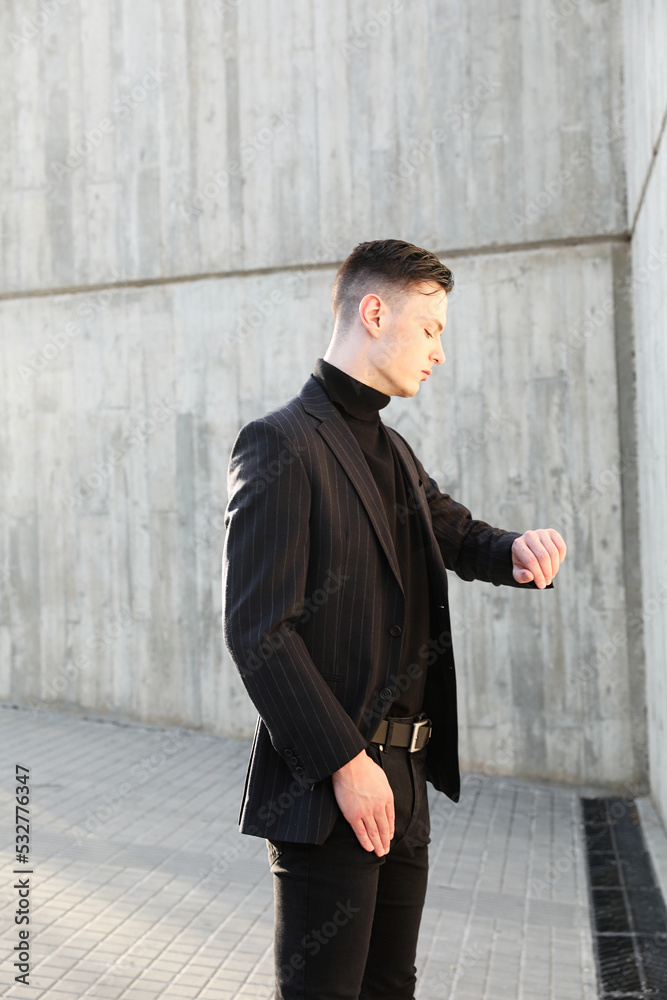 Handsome stylish young man looking at his watch posing outdoor. Vertical. Handsome stylish young man looking at his watch posing outdoor. Vertical.