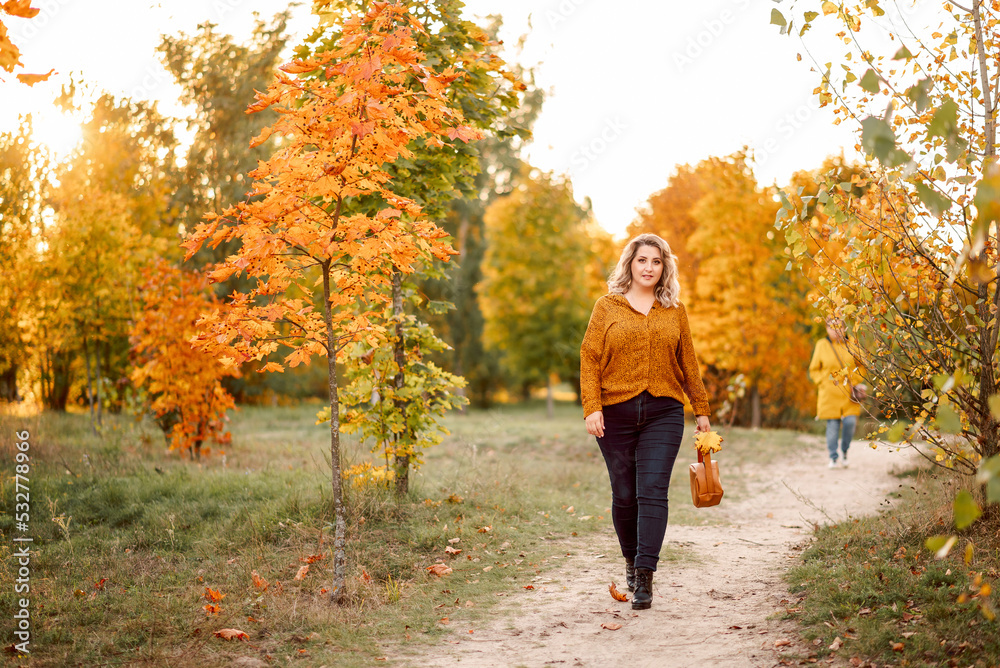 young beautiful plus-size woman in an orange shirt and jeans walks in an autumn park young beautiful plus-size woman in an orange shirt and jeans walks in an autumn park
