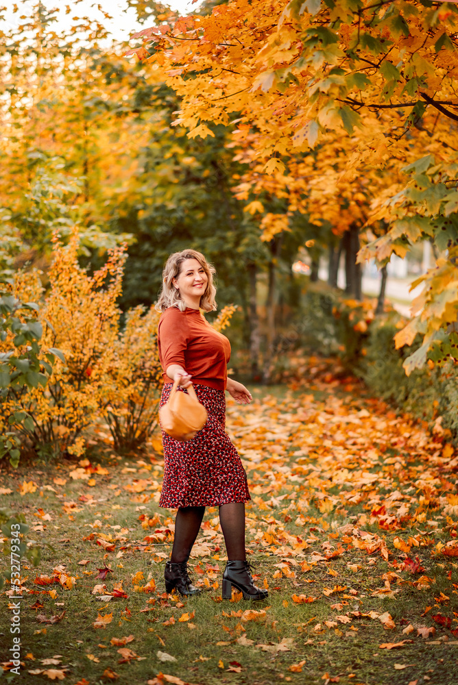 young stylish plus-size woman with a bouquet of yellow leaves walks in an autumn park. Beautiful smiling girl in a brown suit young stylish plus-size woman with a bouquet of yellow leaves walks in an autumn park. Beautiful smiling girl in a brown suit