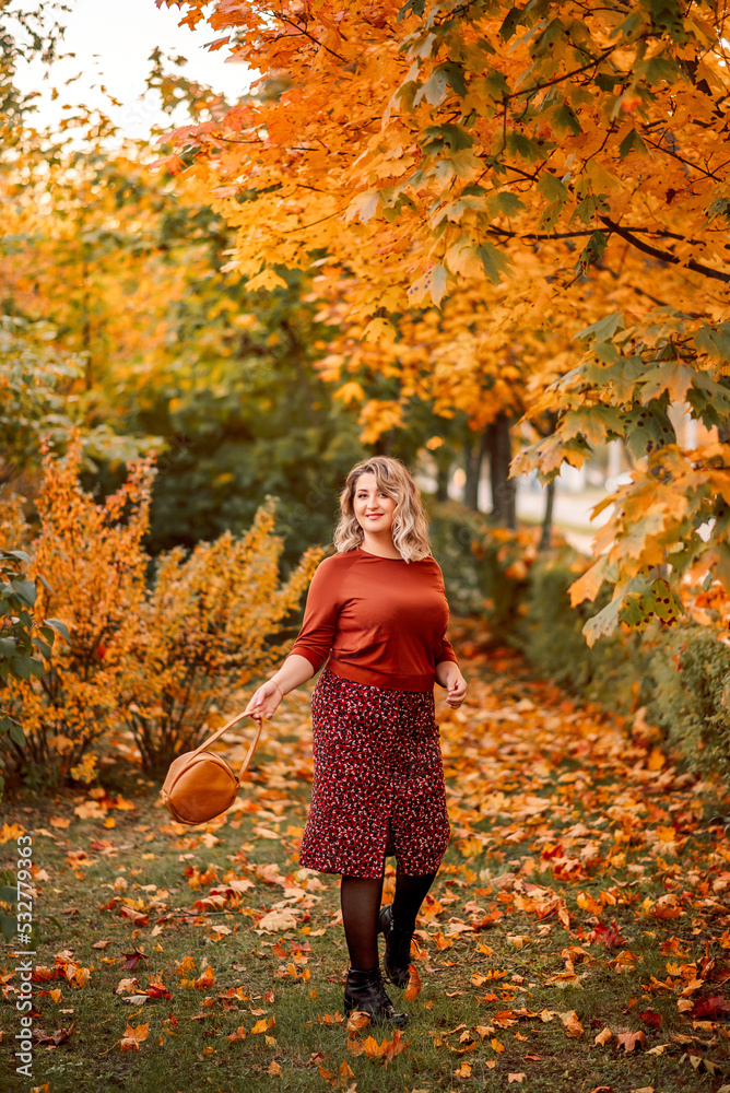 young stylish plus-size woman with a bouquet of yellow leaves walks in an autumn park. Beautiful smiling girl in a brown suit young stylish plus-size woman with a bouquet of yellow leaves walks in an autumn park. Beautiful smiling girl in a brown suit