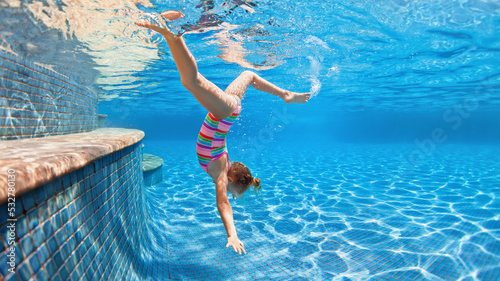 Funny portrait of child learning swimming  dive in blue pool with fun - jumping deep down underwater with splashes. Healthy family lifestyle  kids water sports activity  swimming lesson with parents.
