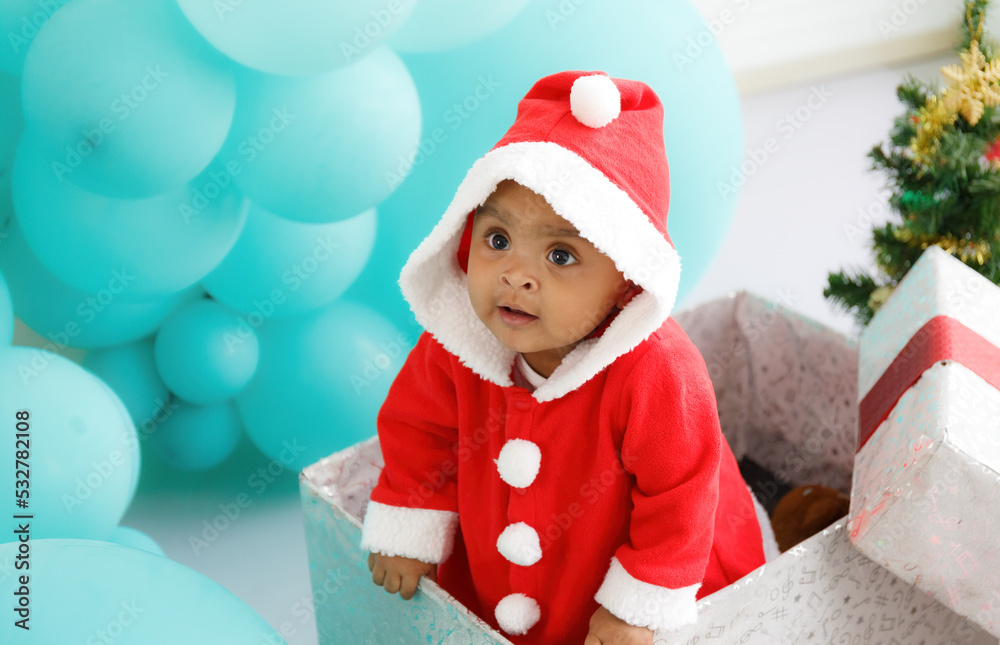 baby girl toddler sitting in a large gift box white background with a Christmas tree, balloons baby girl toddler sitting in a large gift box white background with a Christmas tree, balloons