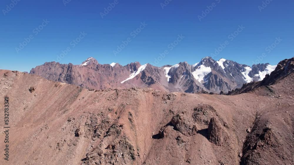 A rocky pass overlooking the snowy mountains. Steep cliffs and big rocks. Blue clear sky. The peaks of the mountains are covered with snow. Top view from a drone. Traces of loose stones. Kazakhstan A rocky pass overlooking the snowy mountains. Steep cliffs and big rocks. Blue clear sky. The peaks of the mountains are covered with snow. Top view from a drone. Traces of loose stones. Kazakhstan