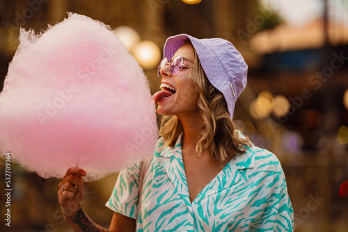 Foto Young white woman eating cotton candy in attraction park
