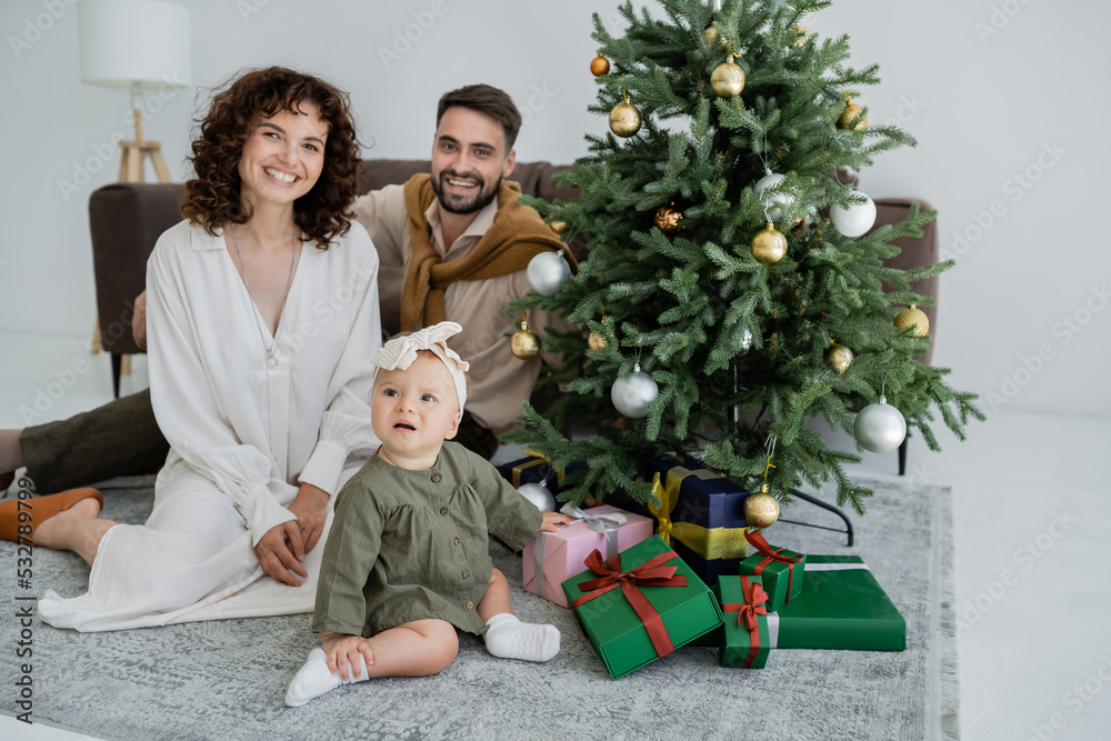 joyful family with infant baby girl sitting near christmas tree with presents. joyful family with infant baby girl sitting near christmas tree with presents.