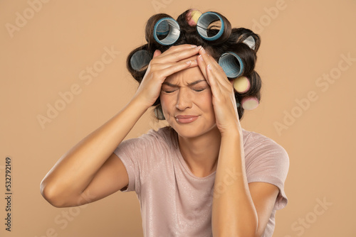 Beautiful woman with hair curlers and headache posing on a beige background © vladimirfloyd