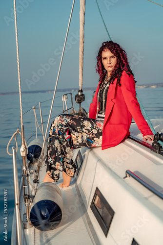 A woman sits on the bow of a yacht on a sunny summer day, the breeze develops her hair, a beautiful sea is in the background